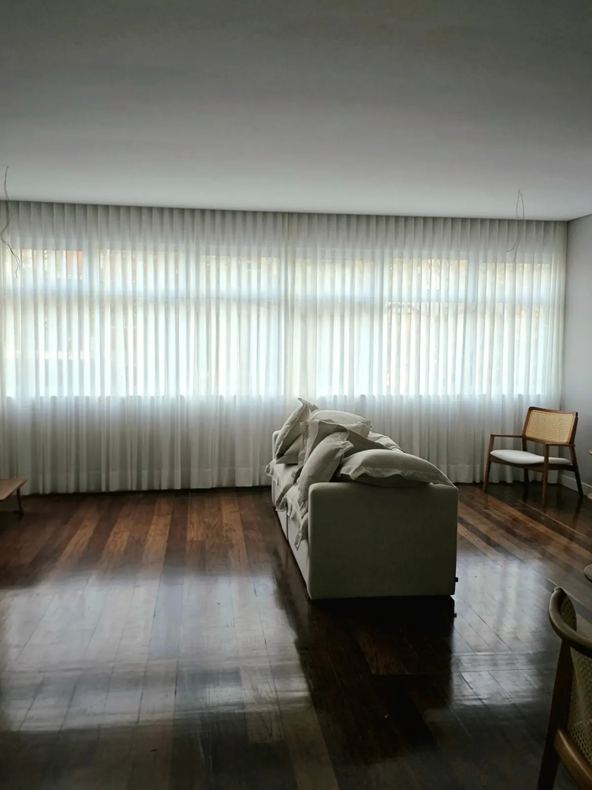 Cortina de voil translúcido em sala com piso de madeira escura
