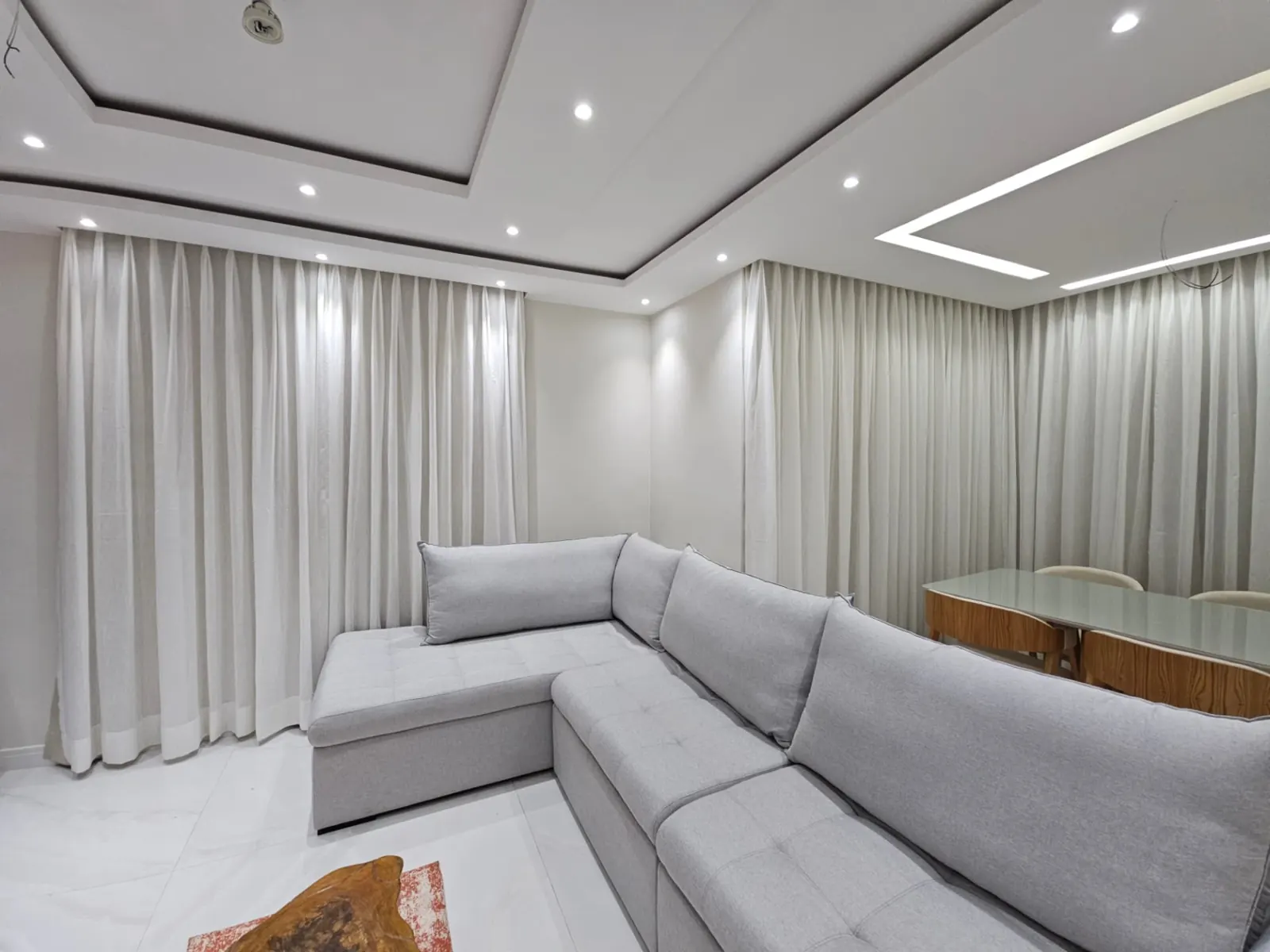 Cortinas claras contornando sala em L com iluminação embutida