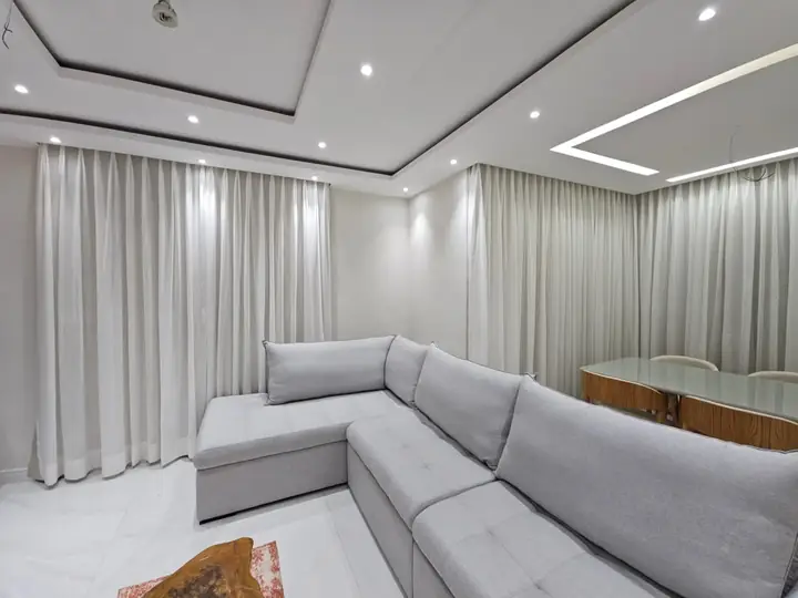 Cortinas claras contornando sala em L com iluminação embutida