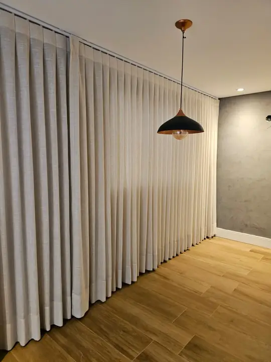 Cortina de pregas em linho cobrindo parede inteira em ambiente amplo